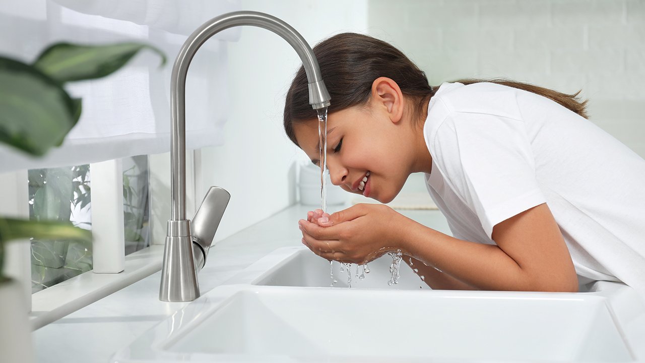 Young girl drinking from the kitchen tap